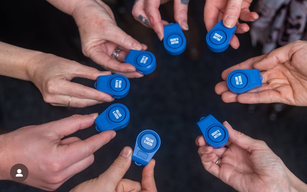 A circle of hands holding blue Becky’s Button personal safety alarms