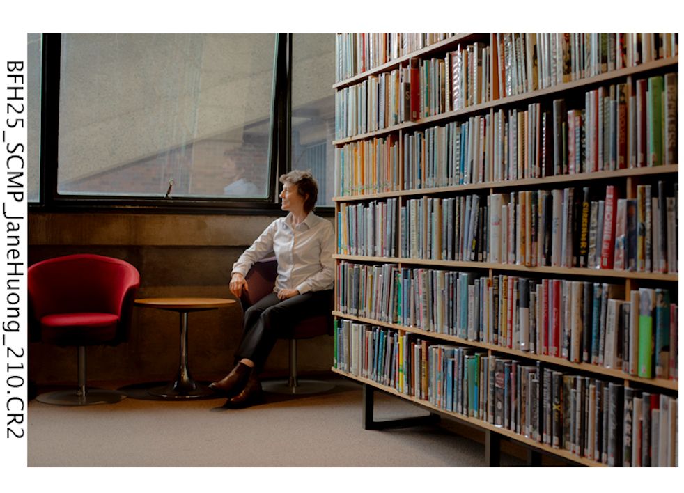 Jane Houng seated in a library beside shelves of books